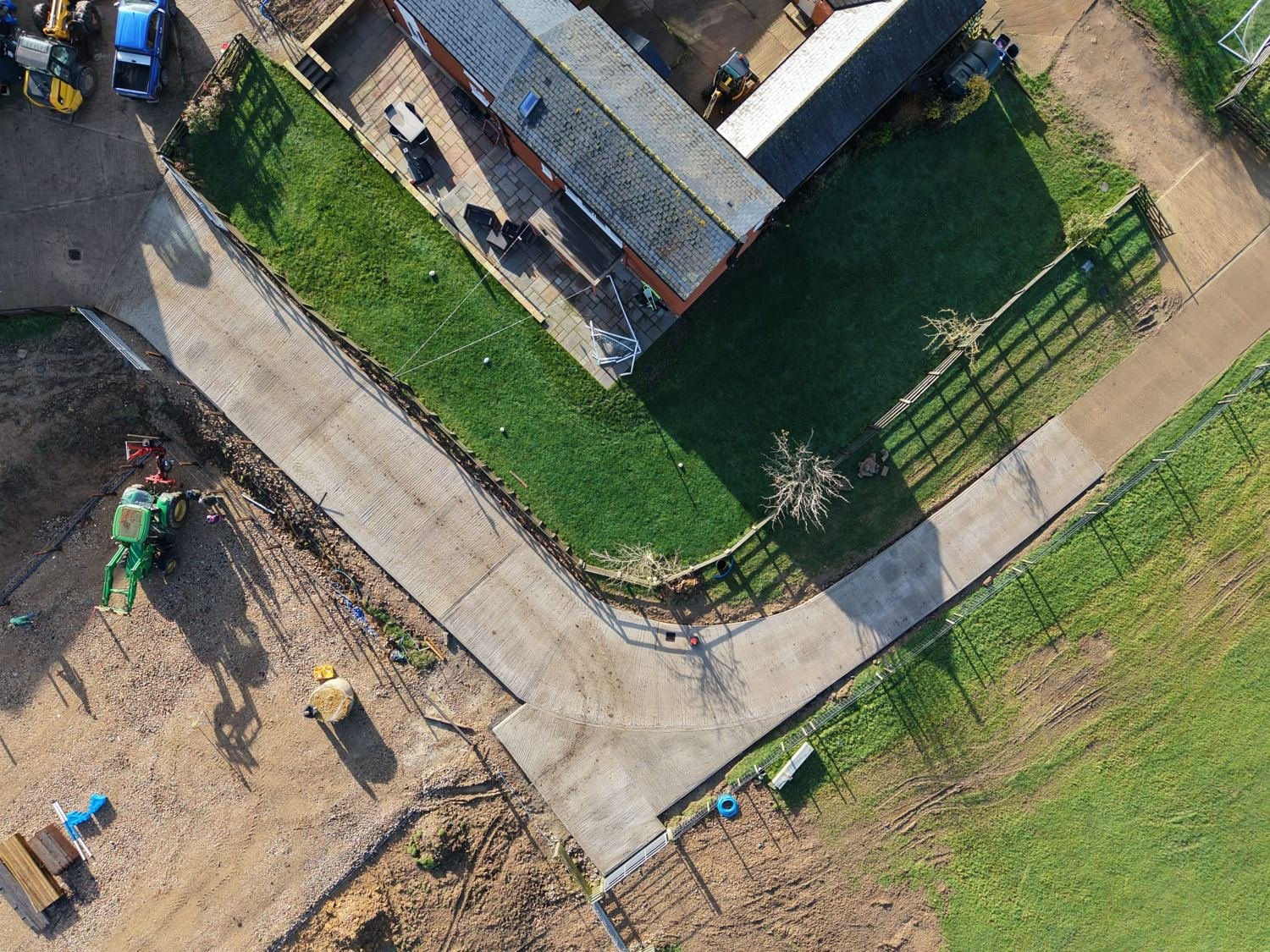 Aerial view of a newly laid concrete drive and farm trackway curving around a house and paddock