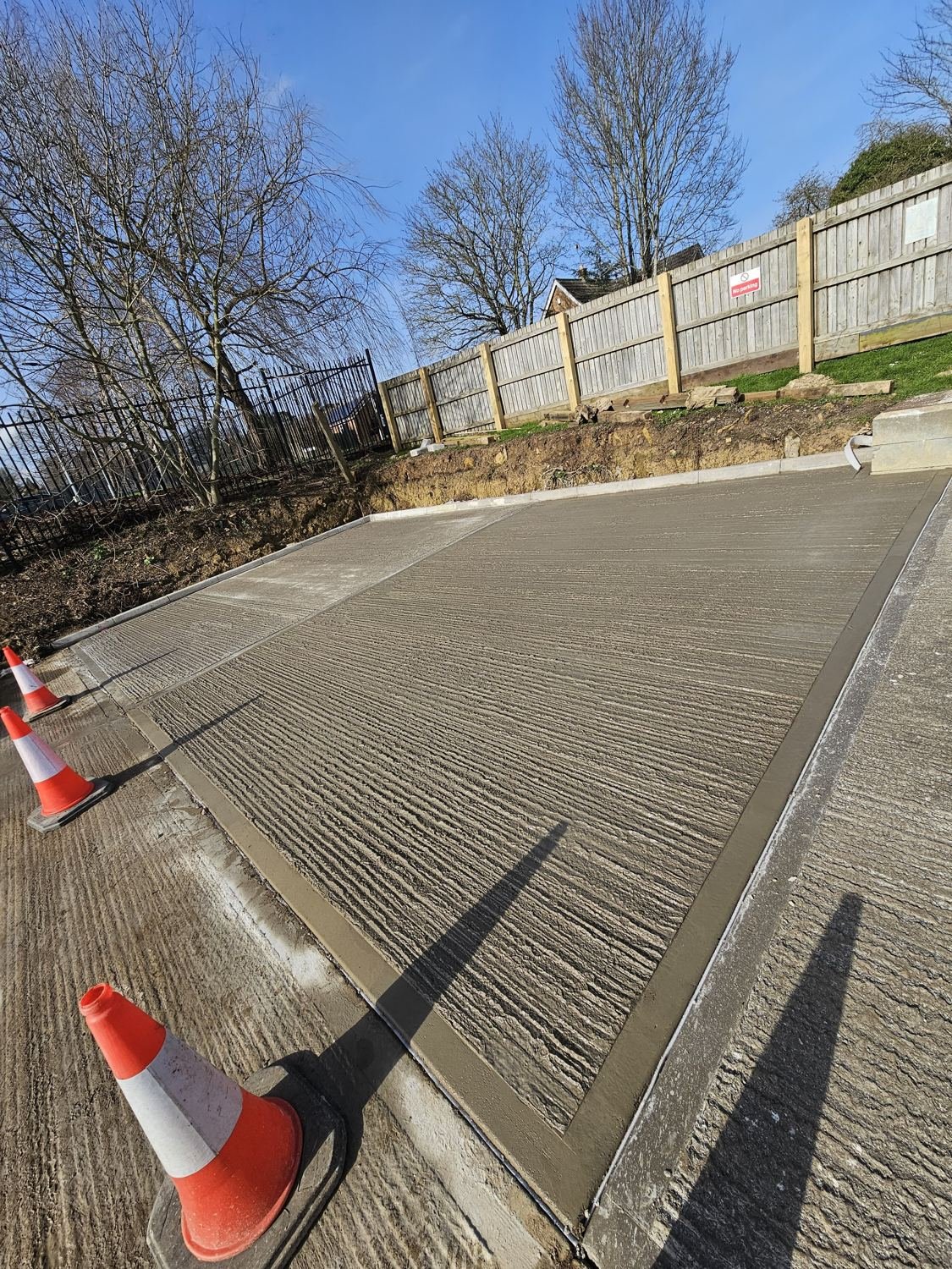 Freshly tamped concrete car park extension edged with kerbs beside an existing car park
