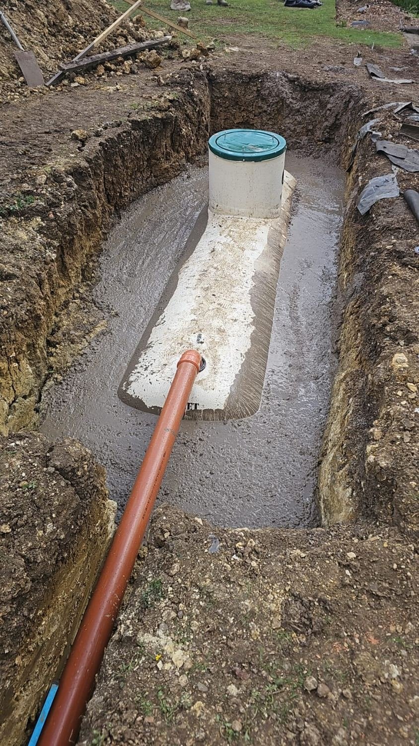 Treatment tank being bedded in concrete in an excavation with an orange drainage pipe